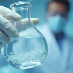 Main gantée tenant une éprouvette en verre remplie de liquide transparent