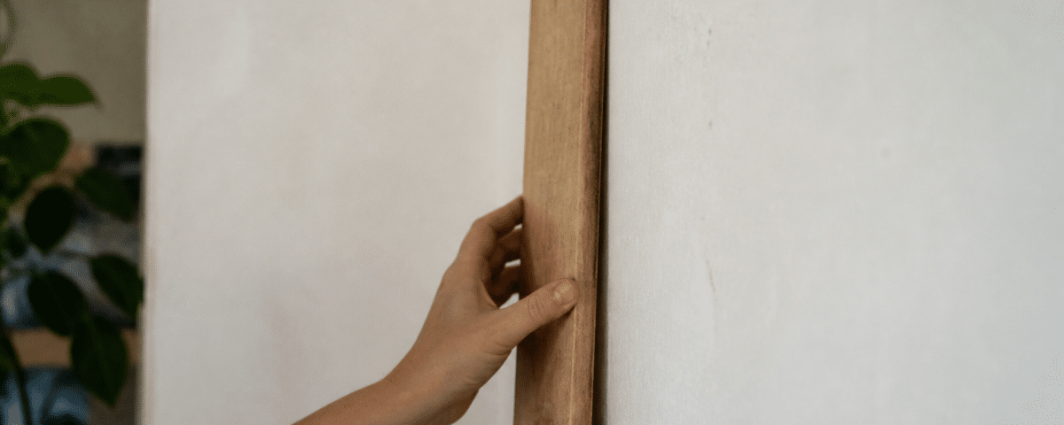 Mains fixant planche bois verticalement sur mur blanc
