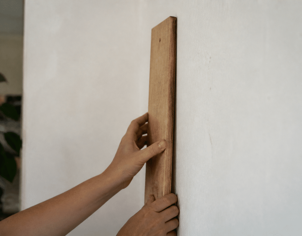 Mains fixant planche bois verticalement sur mur blanc