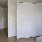 Lit escamotable replié contre mur blanc studio compact