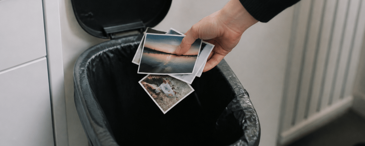 Main jetant des photos imprimees dans une poubelle ouverte